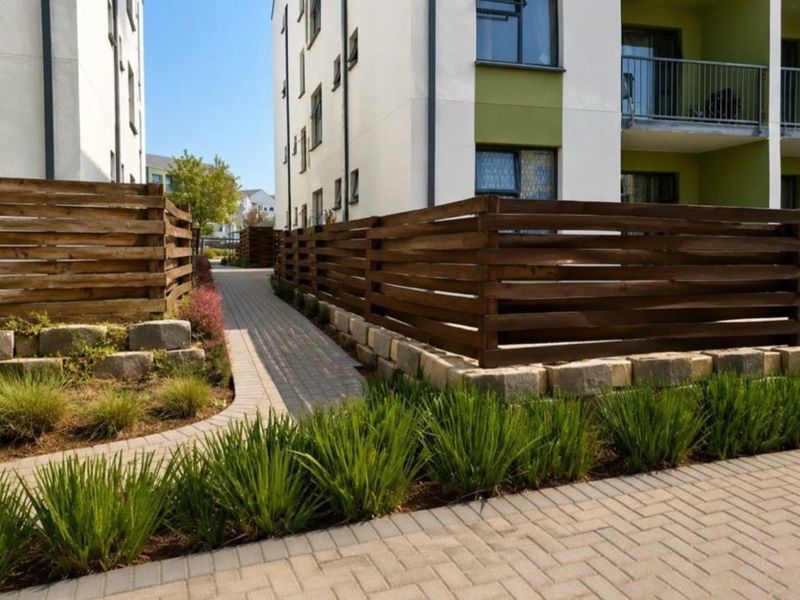 A well-maintained exterior pathway featuring timber slat fencing, paved walkways, and landscaped garden beds between apartment buildings.