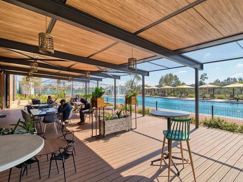 A modern outdoor pool area featuring extensive timber decking, a covered pergola structure, and a well-maintained swimming pool with surrounding landscaping.