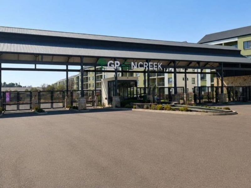 The main entrance and security gatehouse of the apartment complex, featuring a modern metal roof structure and secure perimeter access.