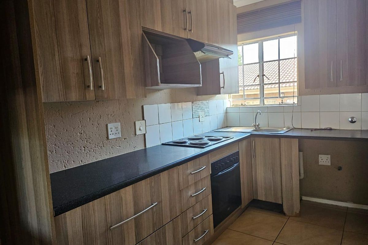A functional kitchen featuring wood-look laminate cabinetry, dark stone countertops, built-in oven, electric hob, and a stainless steel sink with tiled backsplash.