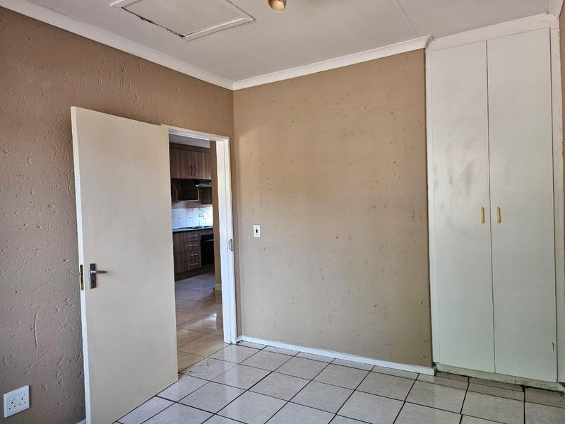 An empty bedroom featuring tiled flooring, a built-in cupboard, and access to an adjacent kitchen area.
