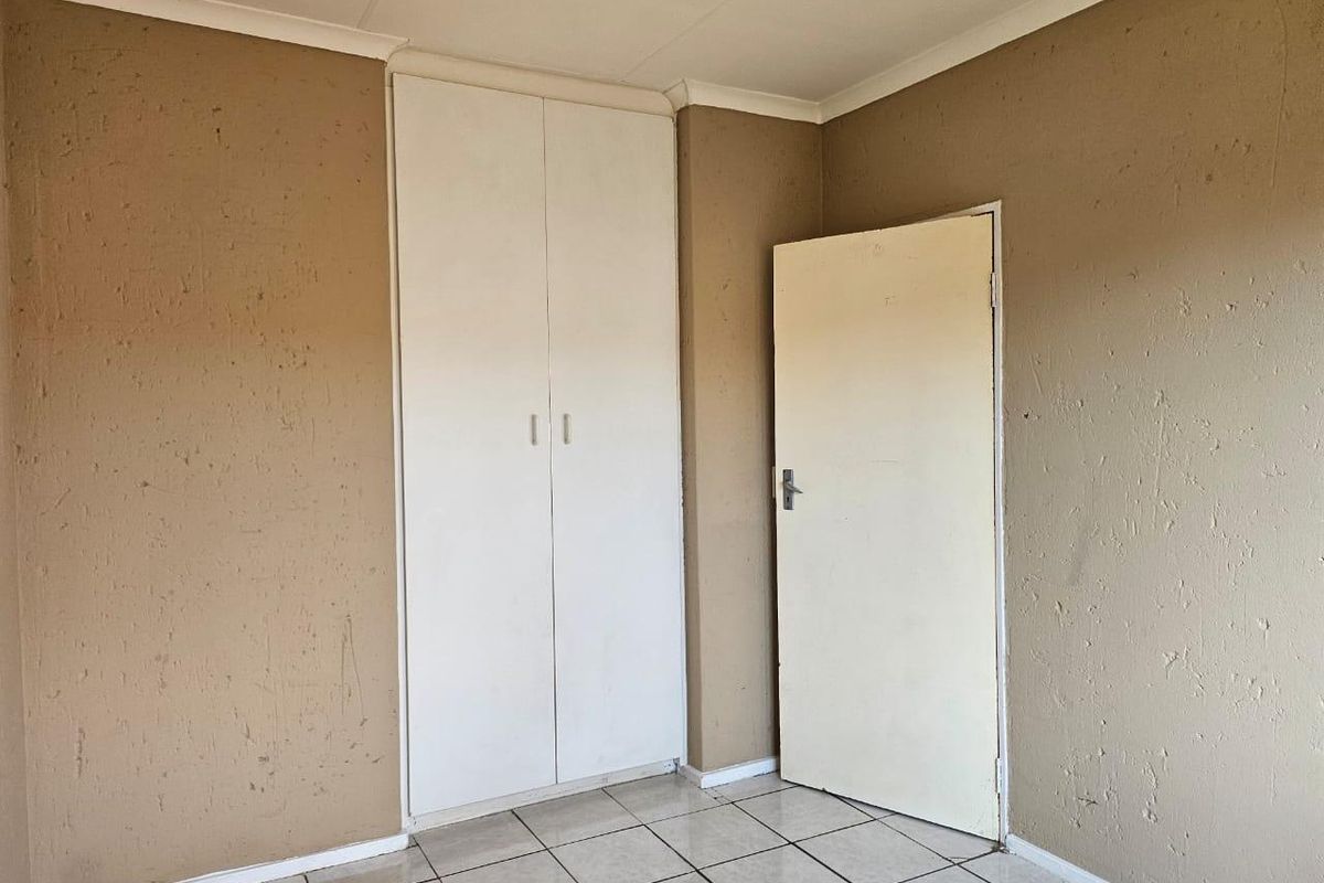An empty bedroom featuring tiled flooring, a built-in cupboard, and neutral wall finishes, offering a blank canvas for renovation or staging.