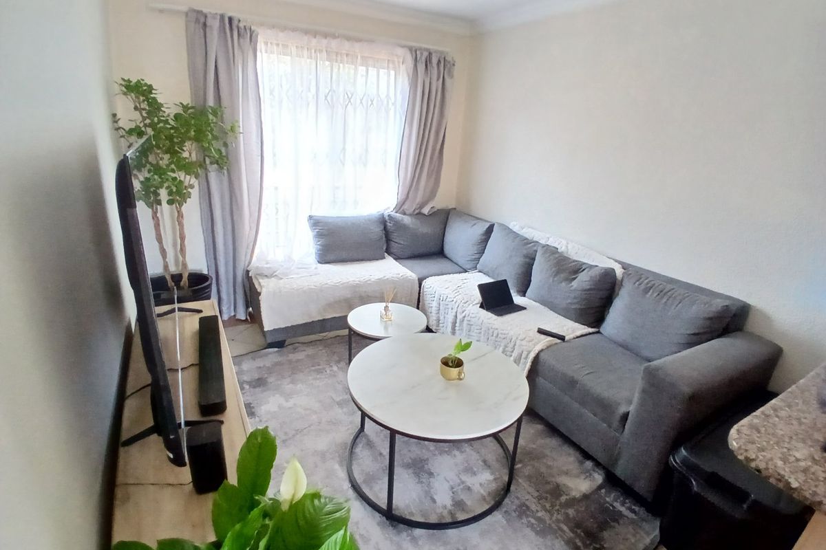 A comfortable living room featuring tiled flooring, coving, and a large window allowing natural light into the space.