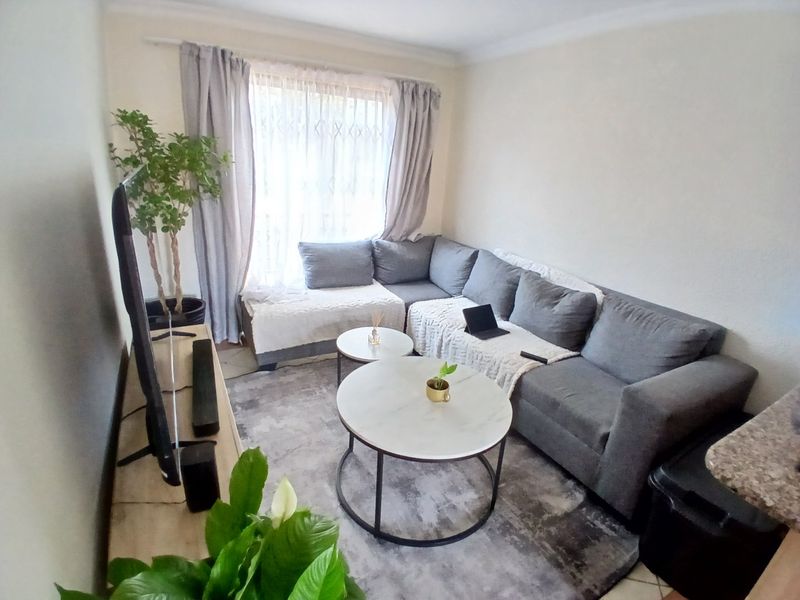 A comfortable living room featuring tiled flooring, coving, and a large window allowing natural light into the space.