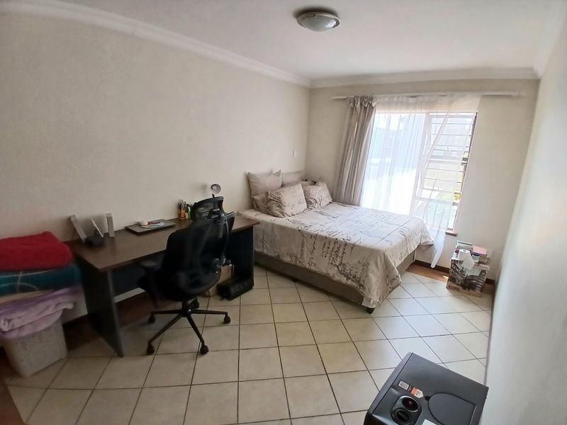 A functional bedroom featuring tiled flooring, a window with security bars, and a ceiling-mounted light fixture.