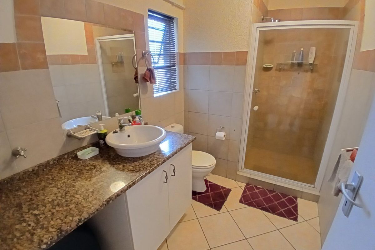 A functional bathroom featuring a granite vanity, ceramic basin, toilet, and a separate shower enclosure with tiled finishes.