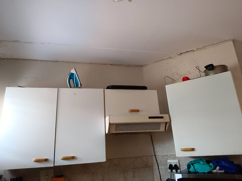 A dated kitchen area featuring white built-in cabinetry, an integrated extractor fan, and tiled backsplash, showing signs of wear and ceiling damage.