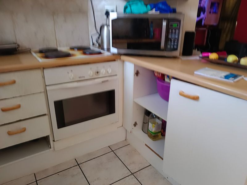 A compact kitchen area featuring a built-in oven, electric hob, laminate countertops, and tiled flooring, currently showing signs of wear and maintenance needs.