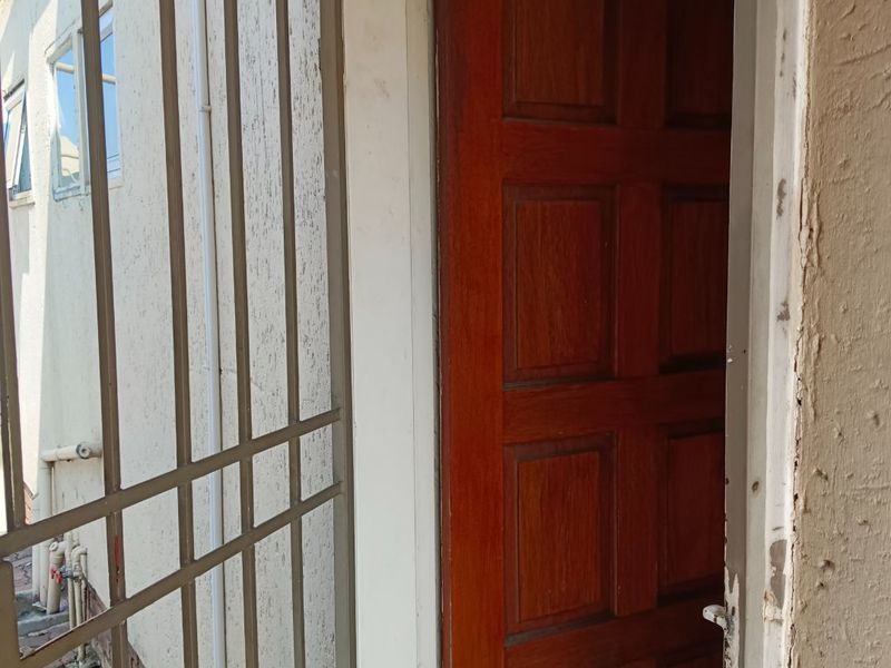 Exterior view of an apartment entrance featuring a security gate and a timber panel door with visible wear on the surrounding wall finish.
