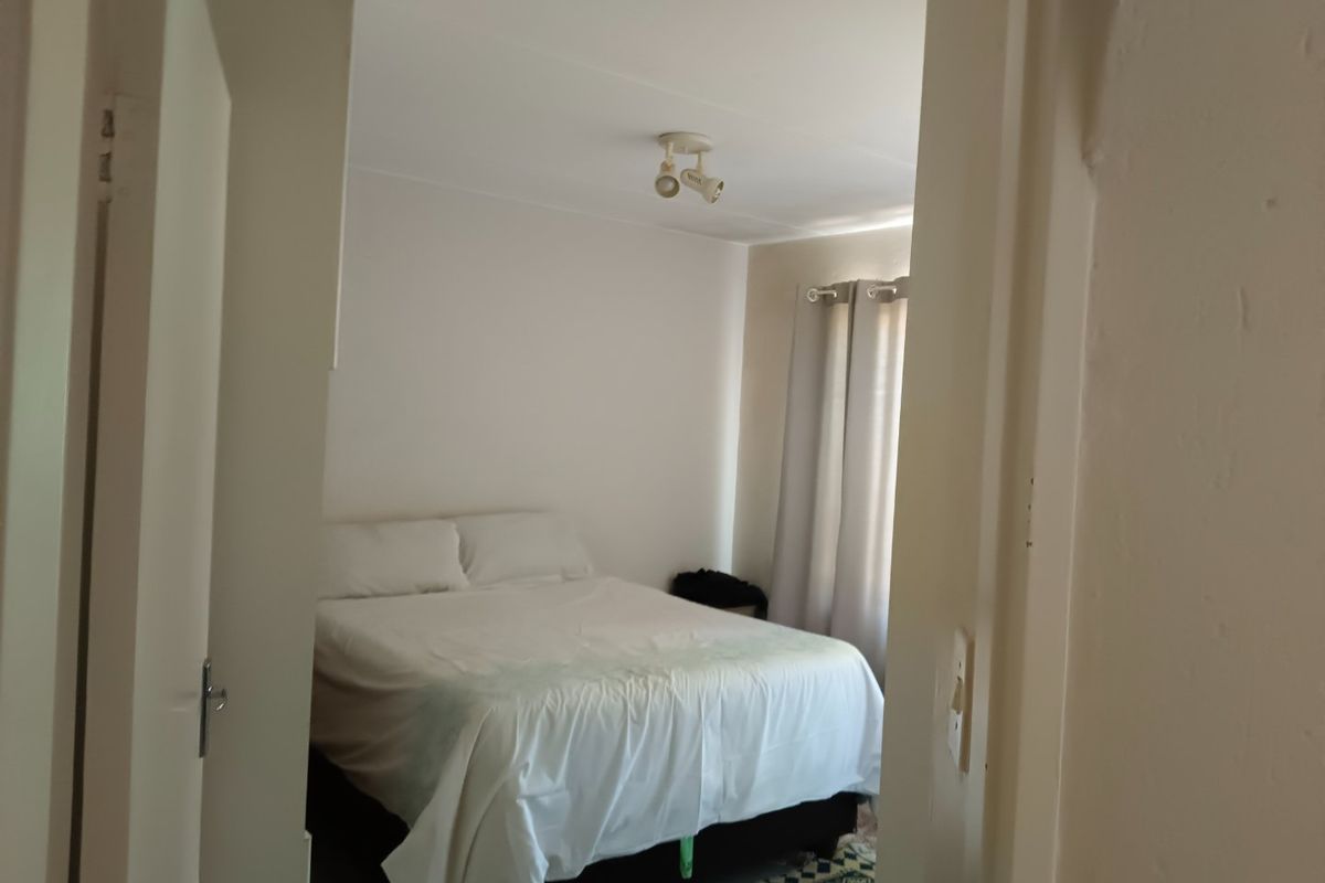A standard bedroom featuring neutral walls, a ceiling-mounted spotlight fixture, and window treatments, viewed from the doorway.
