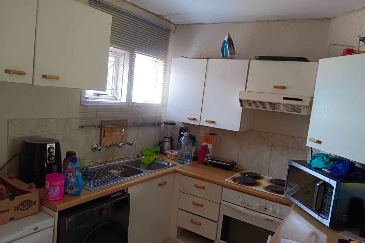 A compact kitchen featuring built-in cabinetry, a double basin sink, and integrated cooking appliances, showing signs of wear and requiring cosmetic updates.