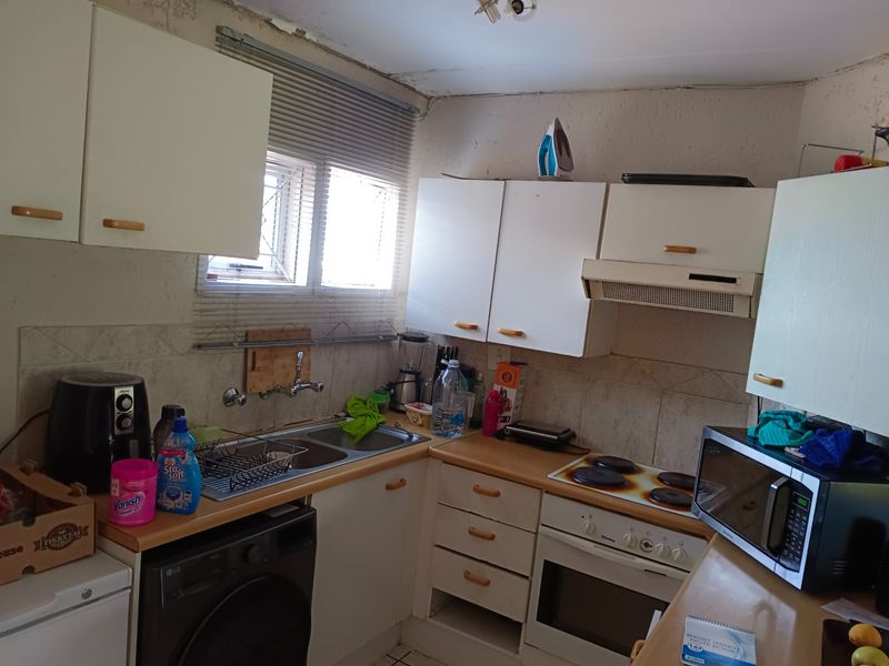 A compact kitchen featuring built-in cabinetry, a double basin sink, and integrated cooking appliances, showing signs of wear and requiring cosmetic updates.