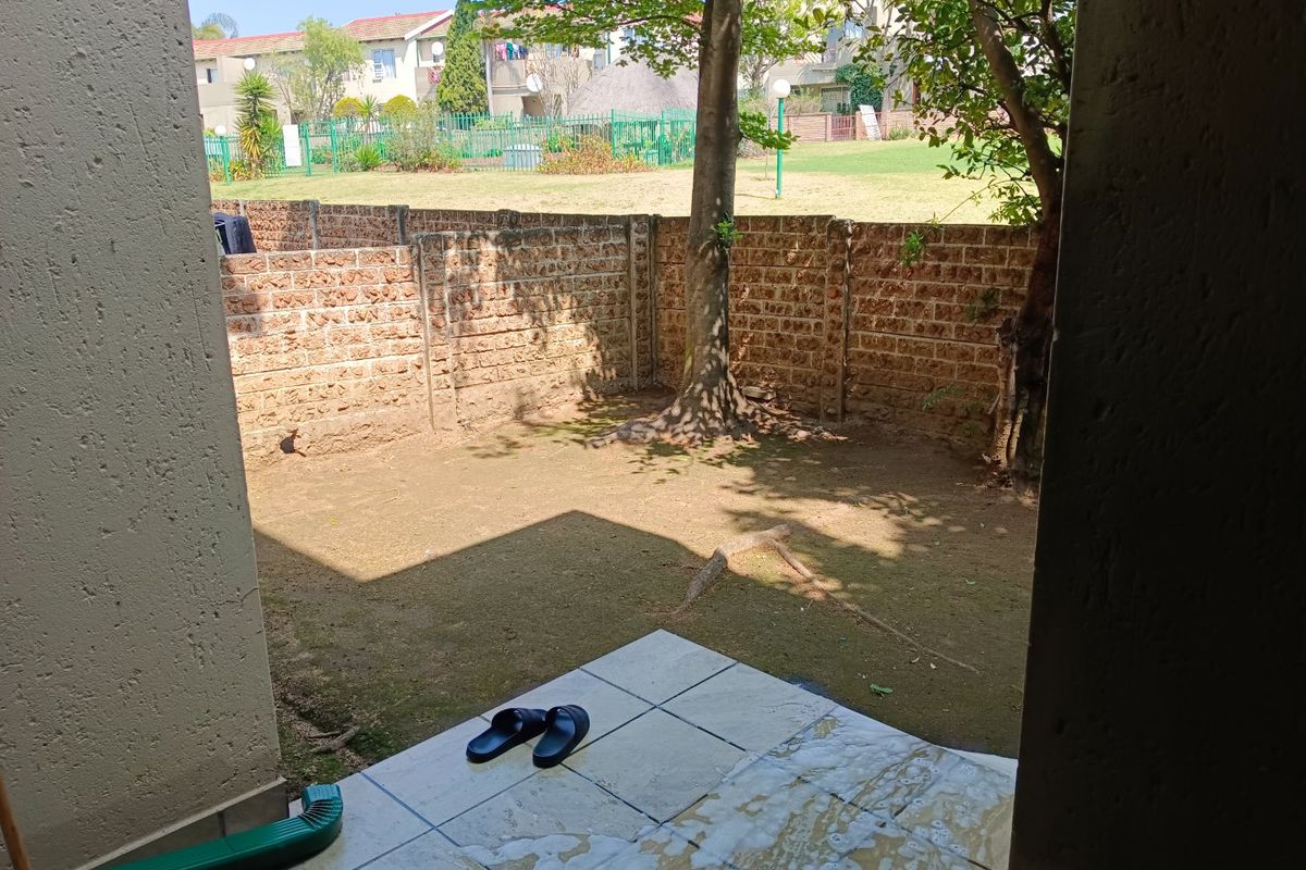 A private rear garden area featuring a tiled patio, brick boundary wall, and established tree, offering potential for landscaping and outdoor living improvements.