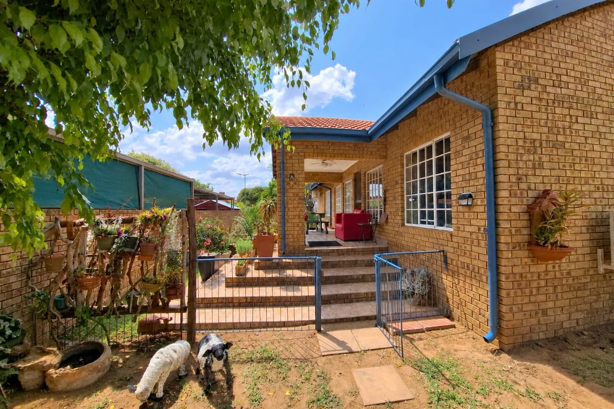 A rear view of the house featuring a face brick facade, a covered tiled patio area, and a metal security gate leading to the garden.
