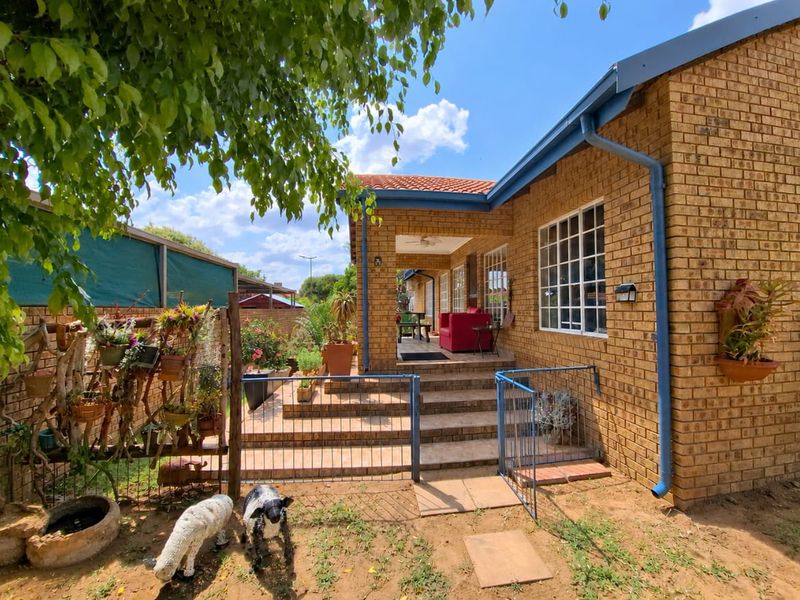 A rear view of the house featuring a face brick facade, a covered tiled patio area, and a metal security gate leading to the garden.