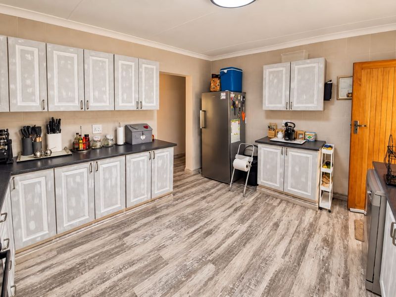A functional kitchen featuring light-toned cabinetry, dark laminate countertops, wood-look flooring, and integrated appliances, offering a practical layout for daily use.
