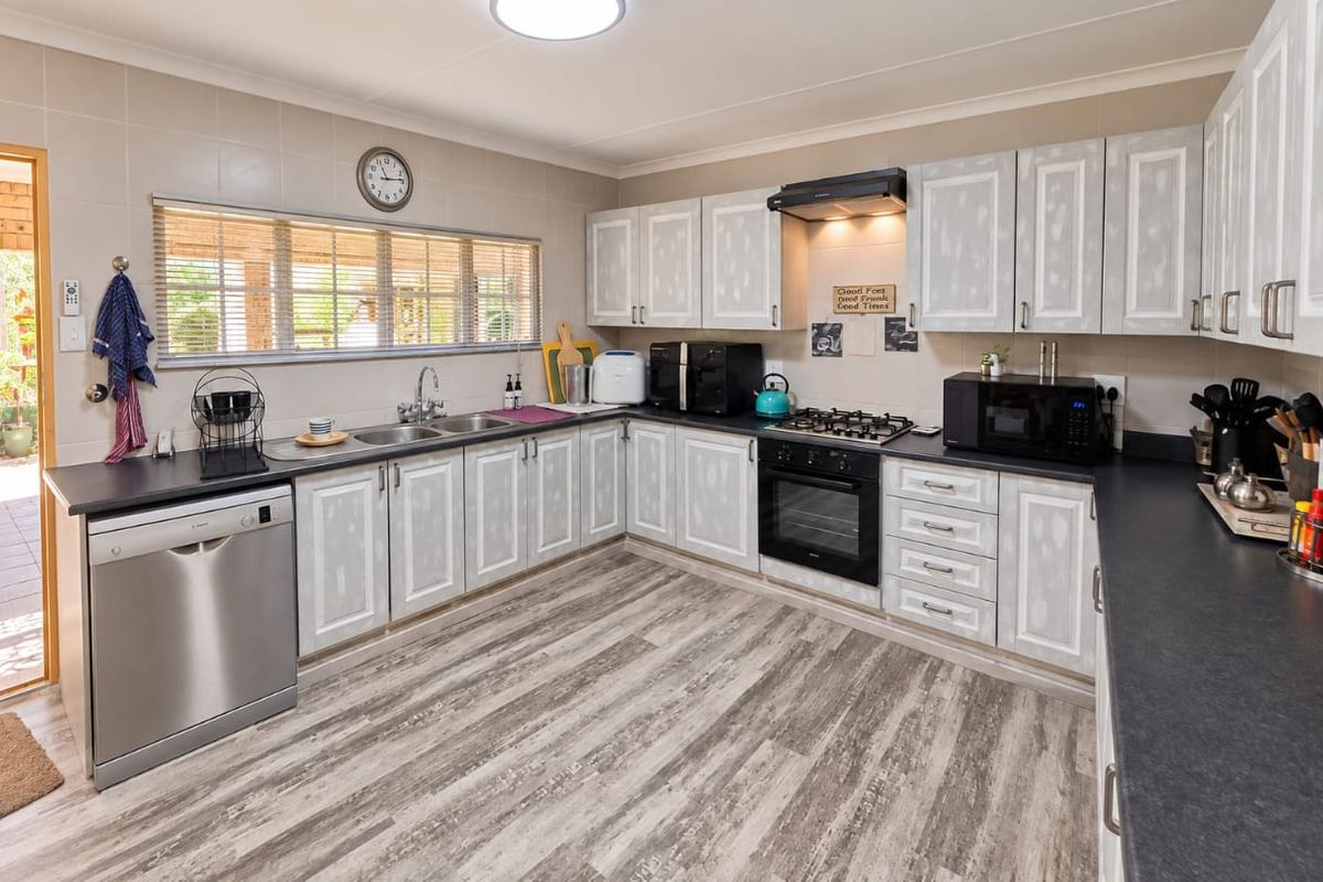 Functional kitchen featuring light-toned cabinetry, dark laminate countertops, built-in oven with gas hob, and durable laminate flooring with direct access to the patio.