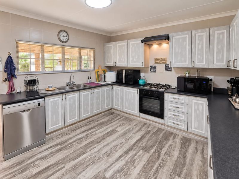 Functional kitchen featuring light-toned cabinetry, dark laminate countertops, built-in oven with gas hob, and durable laminate flooring with direct access to the patio.