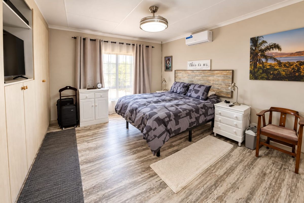 A well-maintained bedroom featuring laminate flooring, built-in cupboards, a ceiling fan, and a wall-mounted split-system air conditioner.