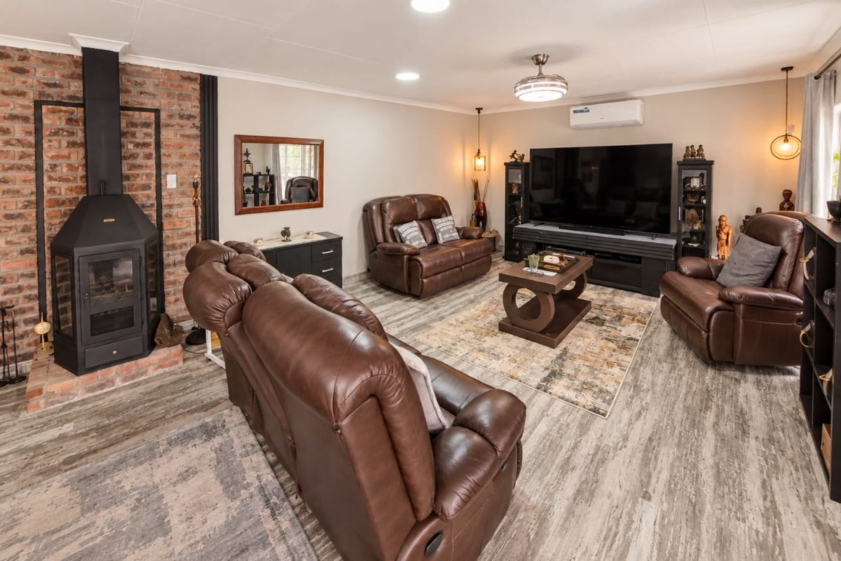 Spacious living room featuring a prominent exposed brick fireplace, modern laminate flooring, and a wall-mounted air conditioning unit.