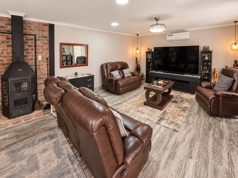 Spacious living room featuring a prominent exposed brick fireplace, modern laminate flooring, and a wall-mounted air conditioning unit.