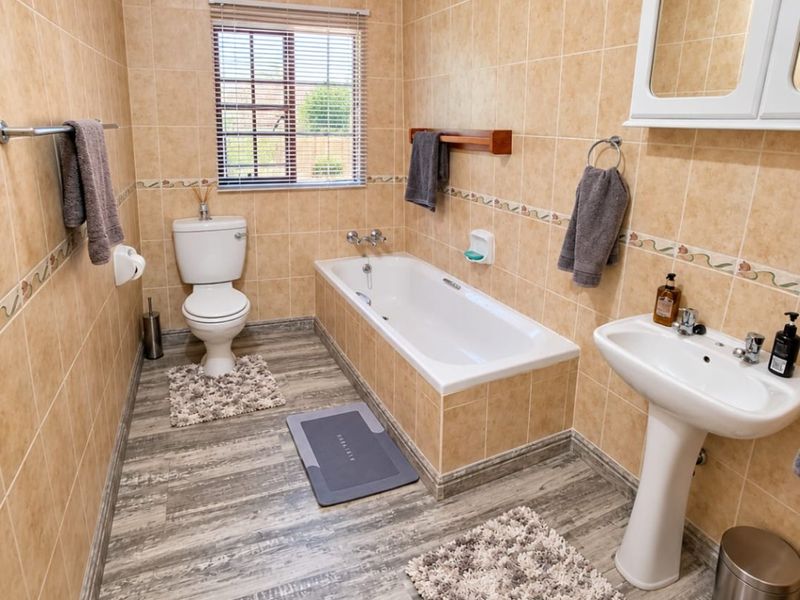 A functional bathroom featuring a pedestal basin, built-in bathtub, and toilet, finished with neutral wall tiles and wood-look laminate flooring.