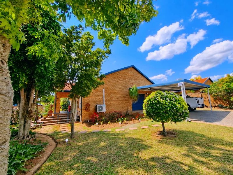 A well-maintained face brick house featuring a landscaped front garden, paved driveway, and a functional carport.