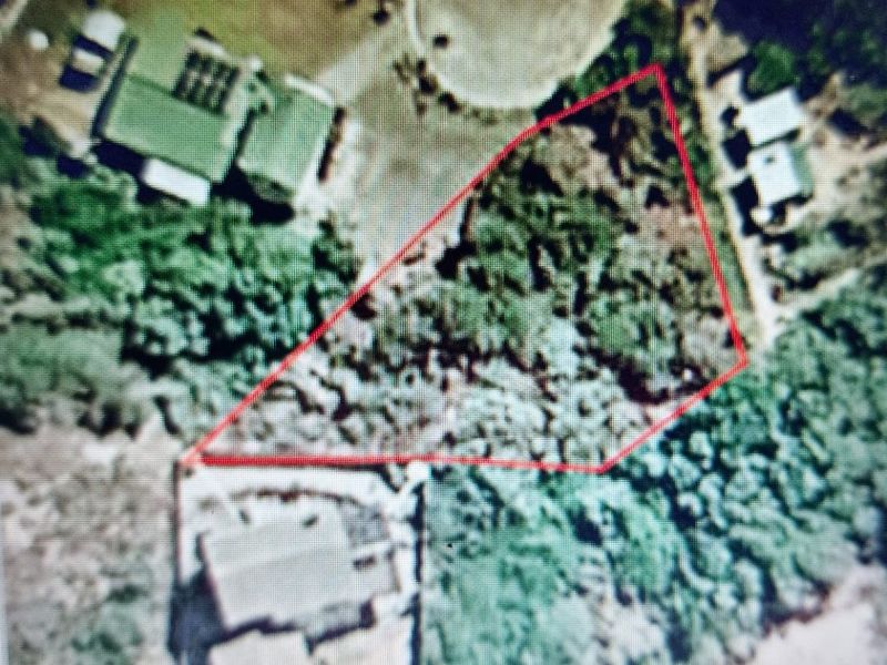 An aerial view of a vacant residential land plot outlined in red, showing surrounding vegetation and neighboring properties.