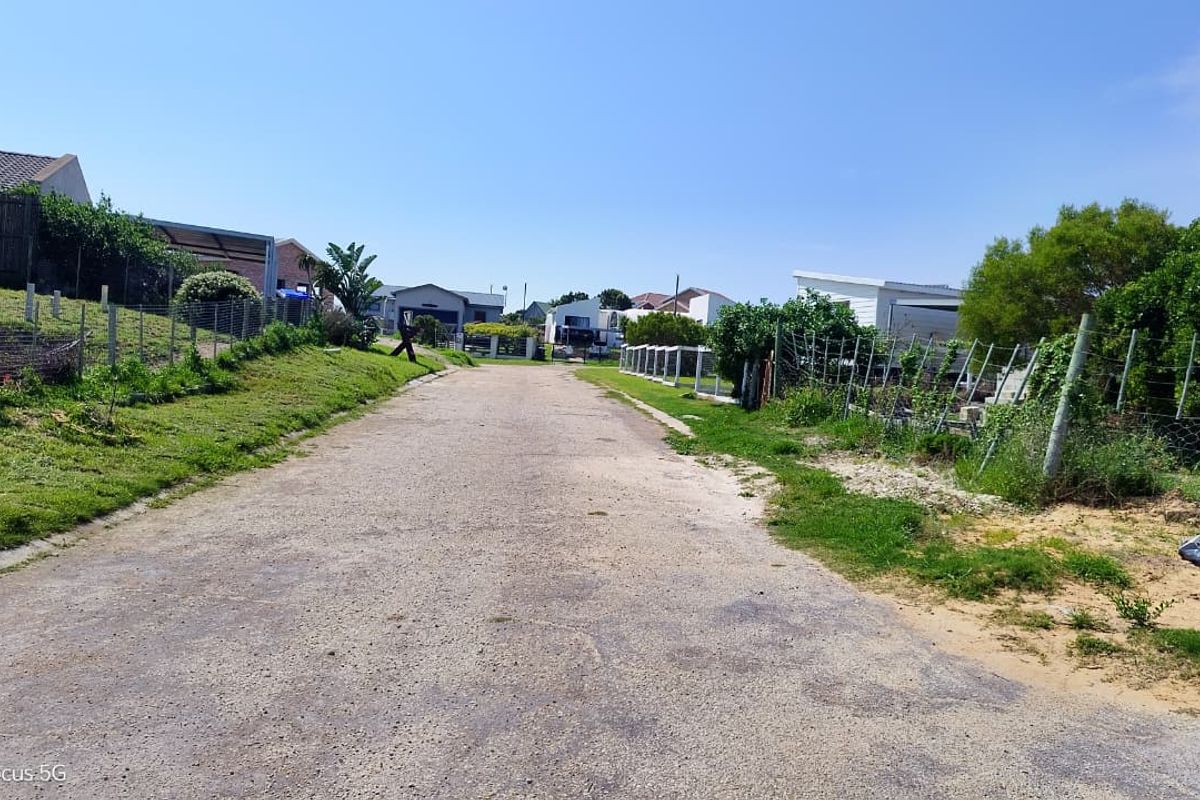 A view of a gravel residential street with surrounding wire fencing and grass verges in a quiet neighborhood setting.