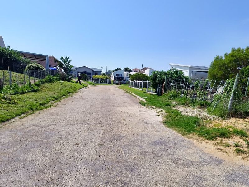 A view of a gravel residential street with surrounding wire fencing and grass verges in a quiet neighborhood setting.