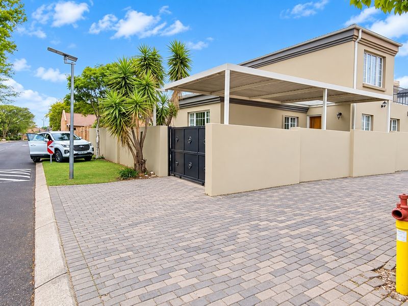 Front exterior view of the property featuring a paved driveway, secure boundary wall with gate, and a covered carport area.
