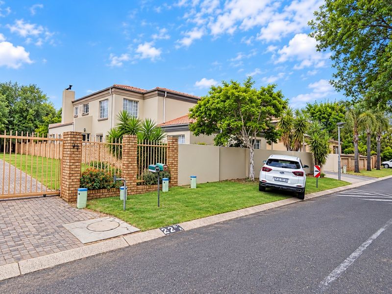 Street view of the property featuring a paved driveway, secure metal gate, and brick boundary wall with established garden.