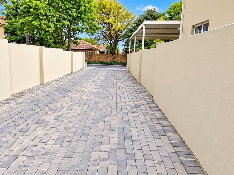A clean, paved driveway leading to the property, flanked by well-maintained boundary walls and featuring a covered carport area.