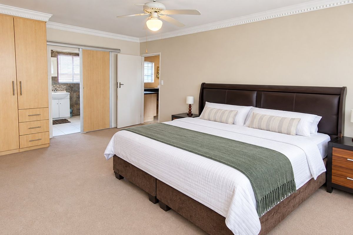 Spacious bedroom featuring neutral carpeting, built-in wooden cupboards, crown molding, a ceiling fan, and direct access to an en-suite bathroom.