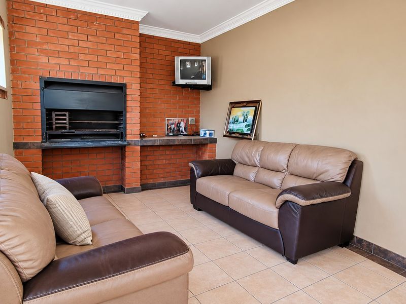 A living area featuring a prominent built-in brick fireplace, tiled flooring, and decorative crown molding.