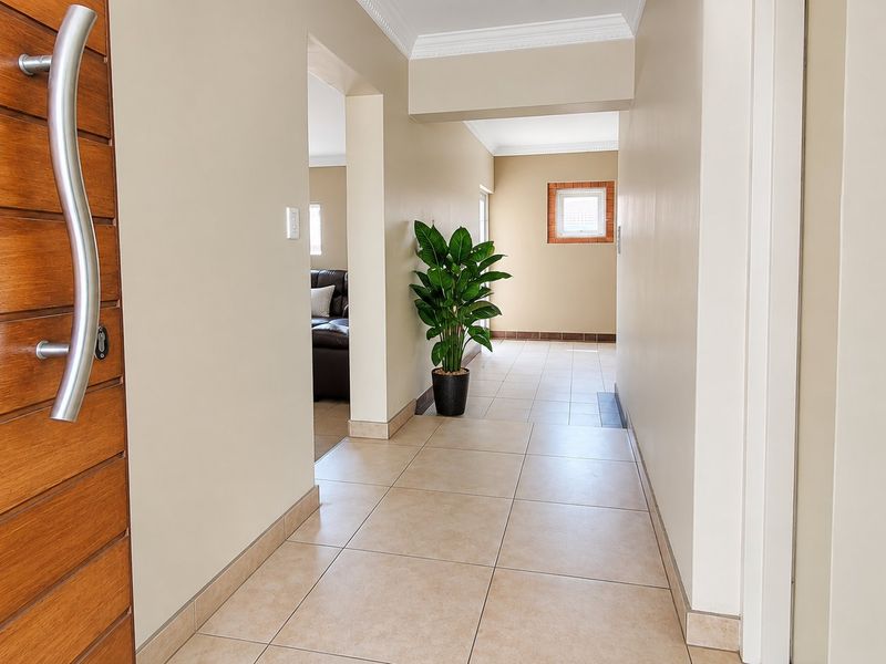 A bright and welcoming entrance hall featuring neutral walls, tiled flooring, and a solid wood front door with a modern stainless steel handle.