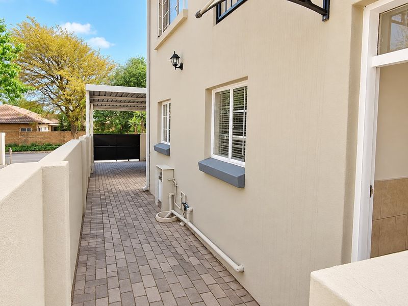 A side exterior view showing a paved walkway, boundary wall, and a carport structure leading to the rear of the property.