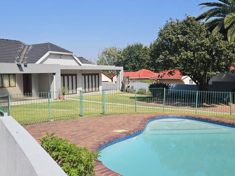 A well-maintained backyard featuring a swimming pool with paved surround, a covered patio area, and established garden space.