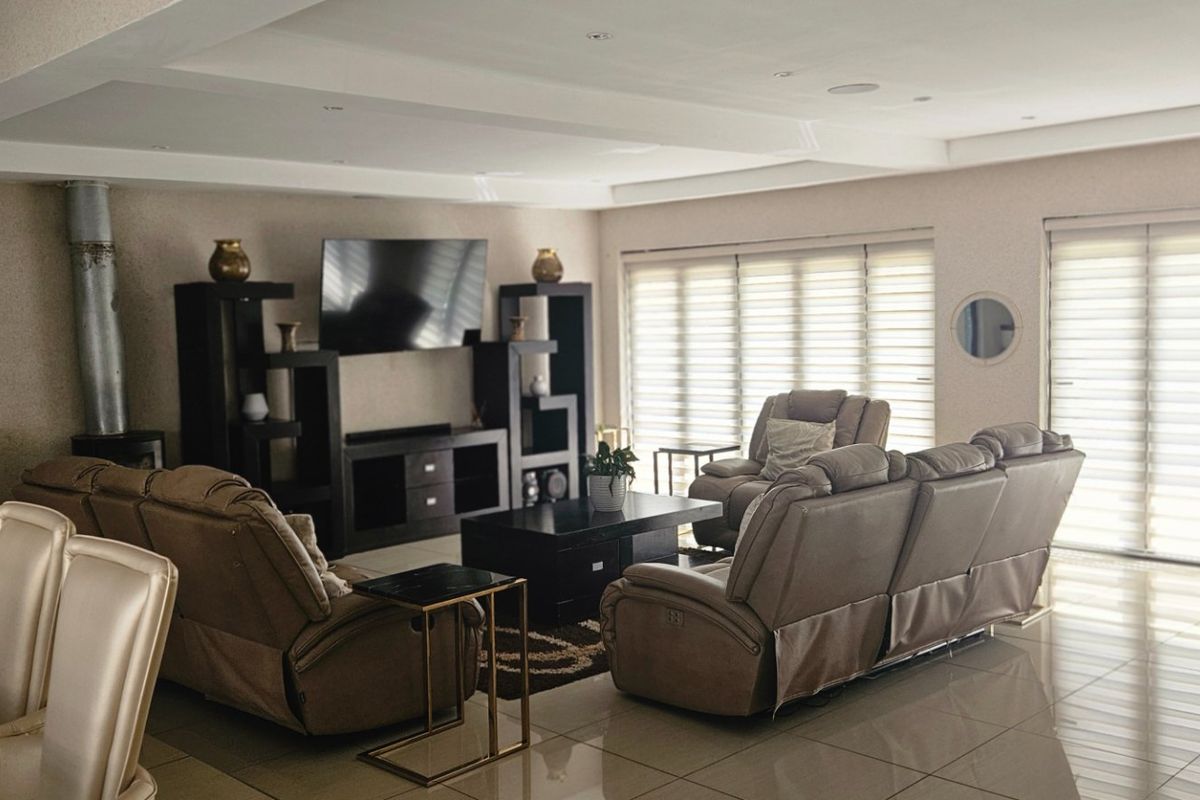 Spacious living area featuring tiled flooring, recessed ceiling lighting, and a built-in wood-burning fireplace, complemented by large windows with fitted roller blinds.