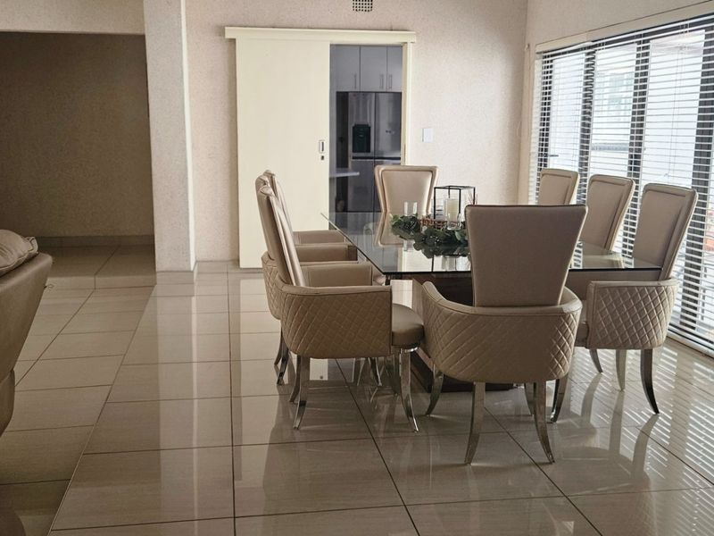 Spacious dining area featuring large windows with blinds, neutral tiled flooring, and a sliding door leading to the kitchen area.