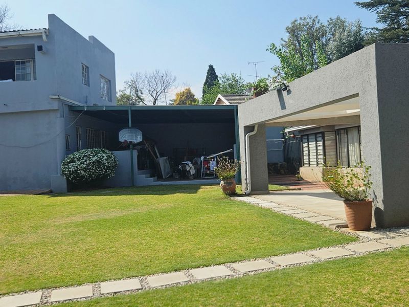 Rear view of the property featuring a spacious lawn, a covered patio area, and a detached carport structure.