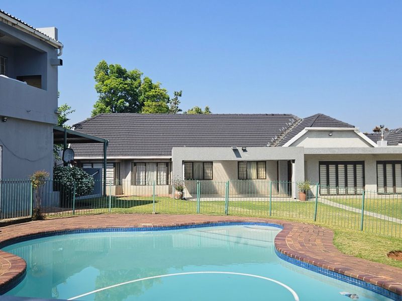A well-maintained backyard featuring a swimming pool with brick coping, a grassy lawn, and a covered patio area attached to the main house.