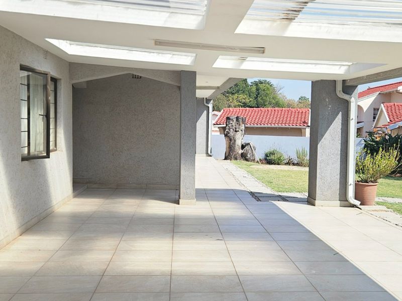 A spacious covered patio featuring tiled flooring and translucent roof panels, providing a bright, versatile outdoor living area overlooking the garden.