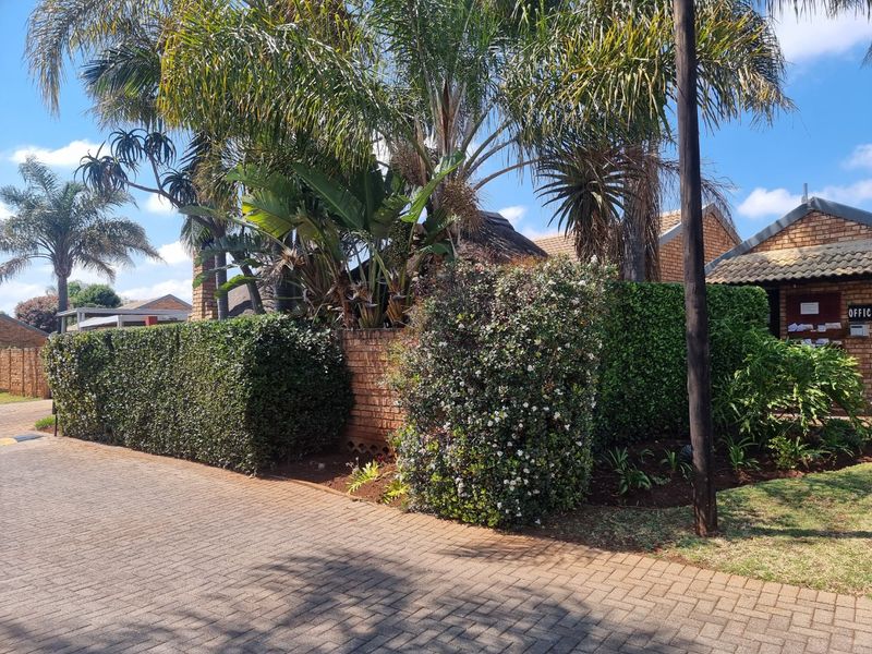 Front view of the townhouse complex entrance featuring brick paving, established garden landscaping, and traditional brick and thatch architectural elements.