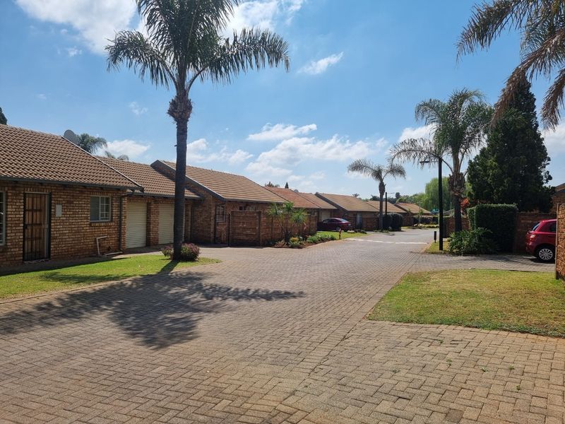 A view of the townhouse complex featuring brick facades, tiled roofs, and a paved driveway leading to individual garage entrances.