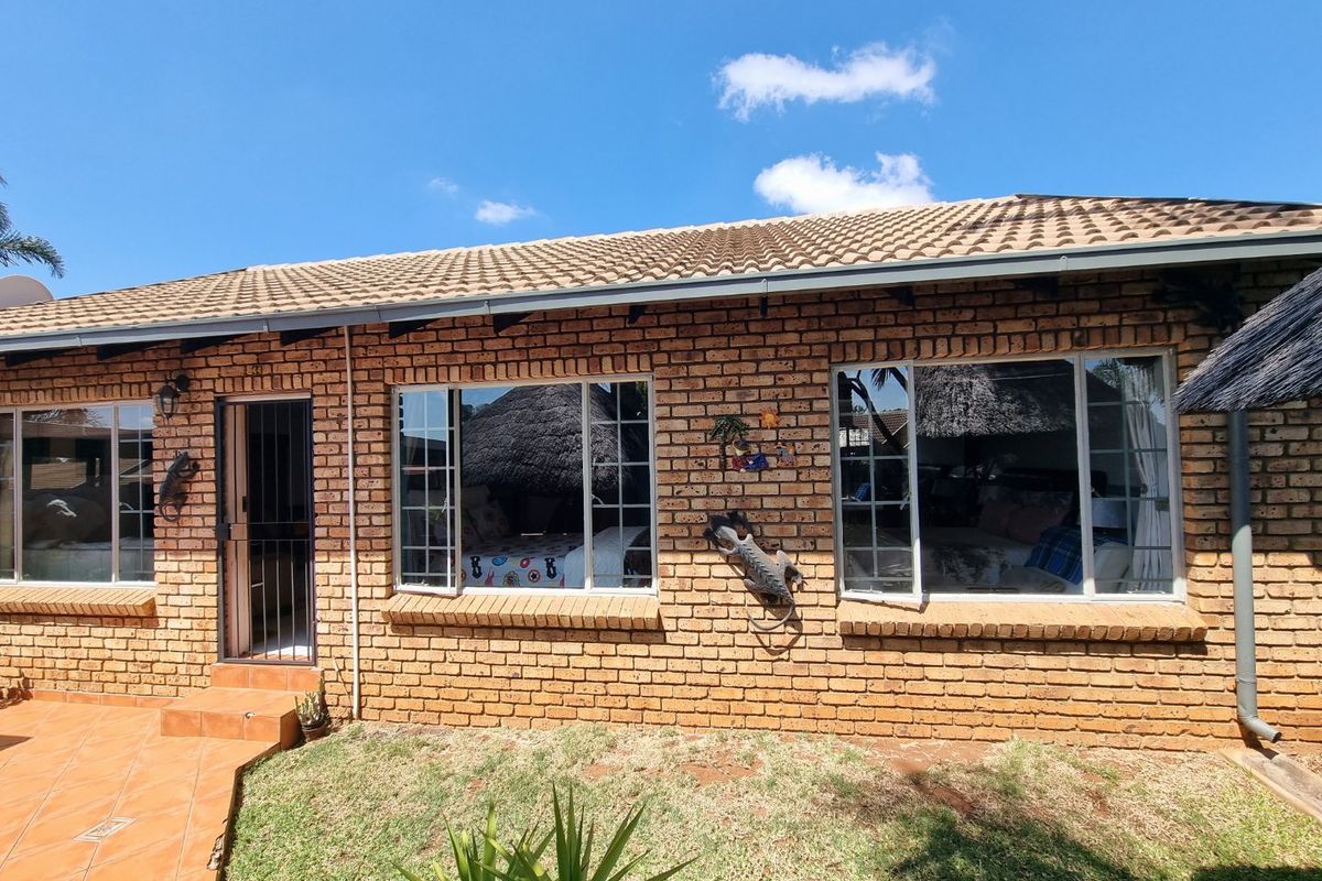 Rear exterior view of a face brick townhouse featuring a tiled roof, aluminium window frames, and a small tiled patio area.