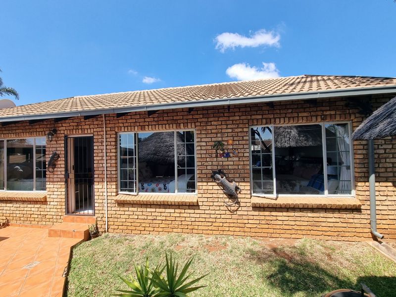Rear exterior view of a face brick townhouse featuring a tiled roof, aluminium window frames, and a small tiled patio area.