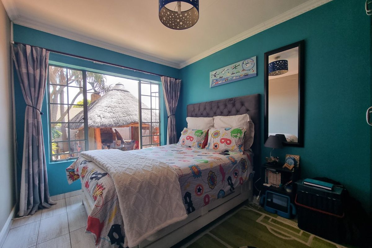 A well-lit bedroom featuring tiled flooring, a large window with garden views, and decorative cornice detailing.