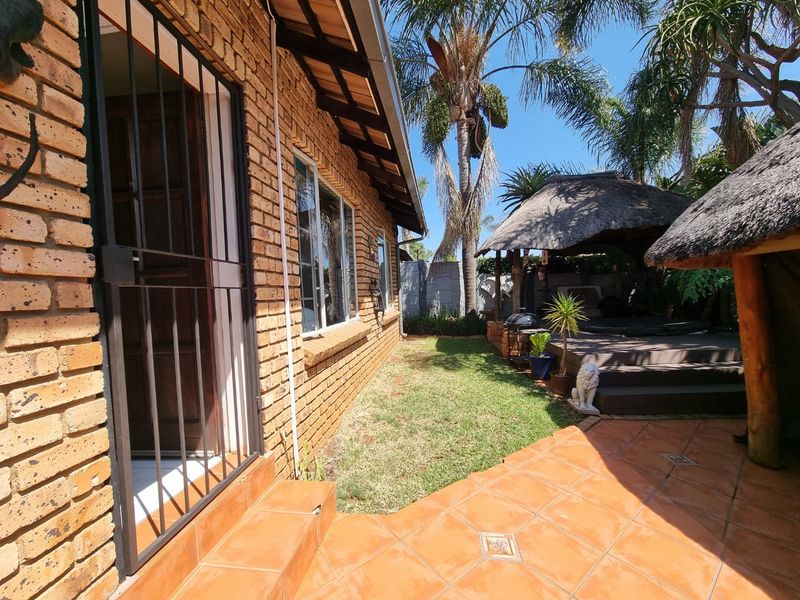Rear exterior view of the townhouse featuring a face brick facade, a tiled patio area, and a thatched lapa with a raised timber deck.