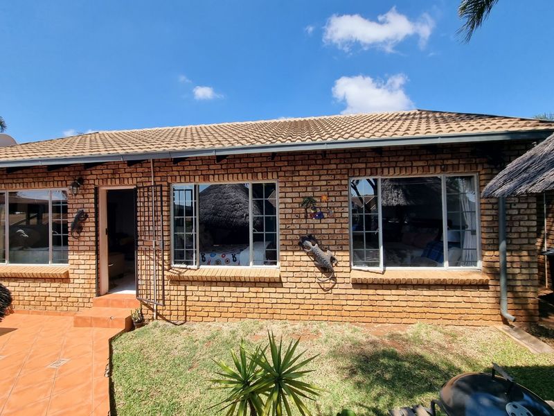 Rear exterior view of a face brick townhouse featuring a tiled roof, aluminium windows, and a paved patio area.